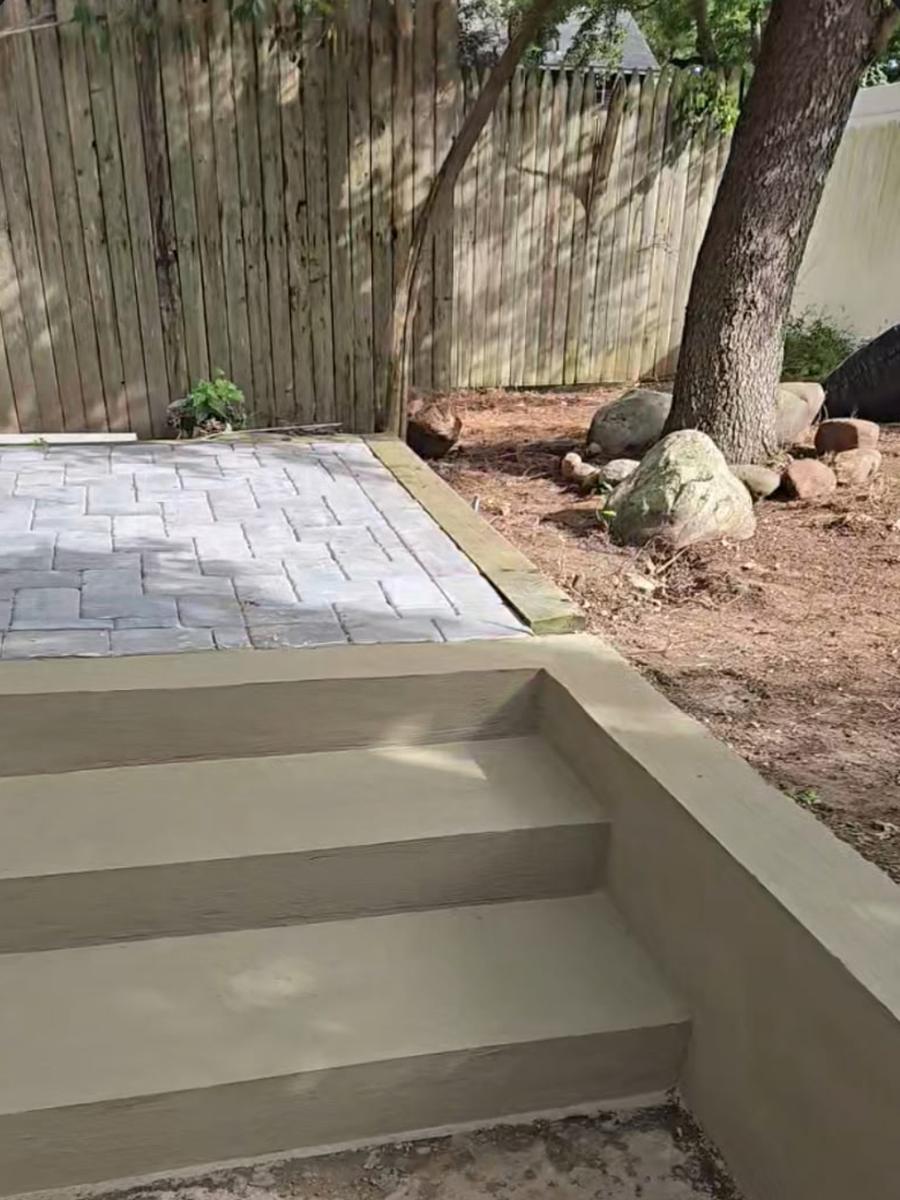 After: new stucco retaining wall and concrete steps leading to a paver patio
